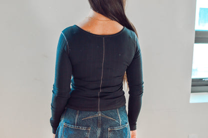 Person wearing a black long-sleeve top and blue jeans from behind on a plain background