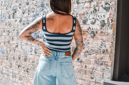 Person wearing a striped tank top and denim shorts against a brick wall.