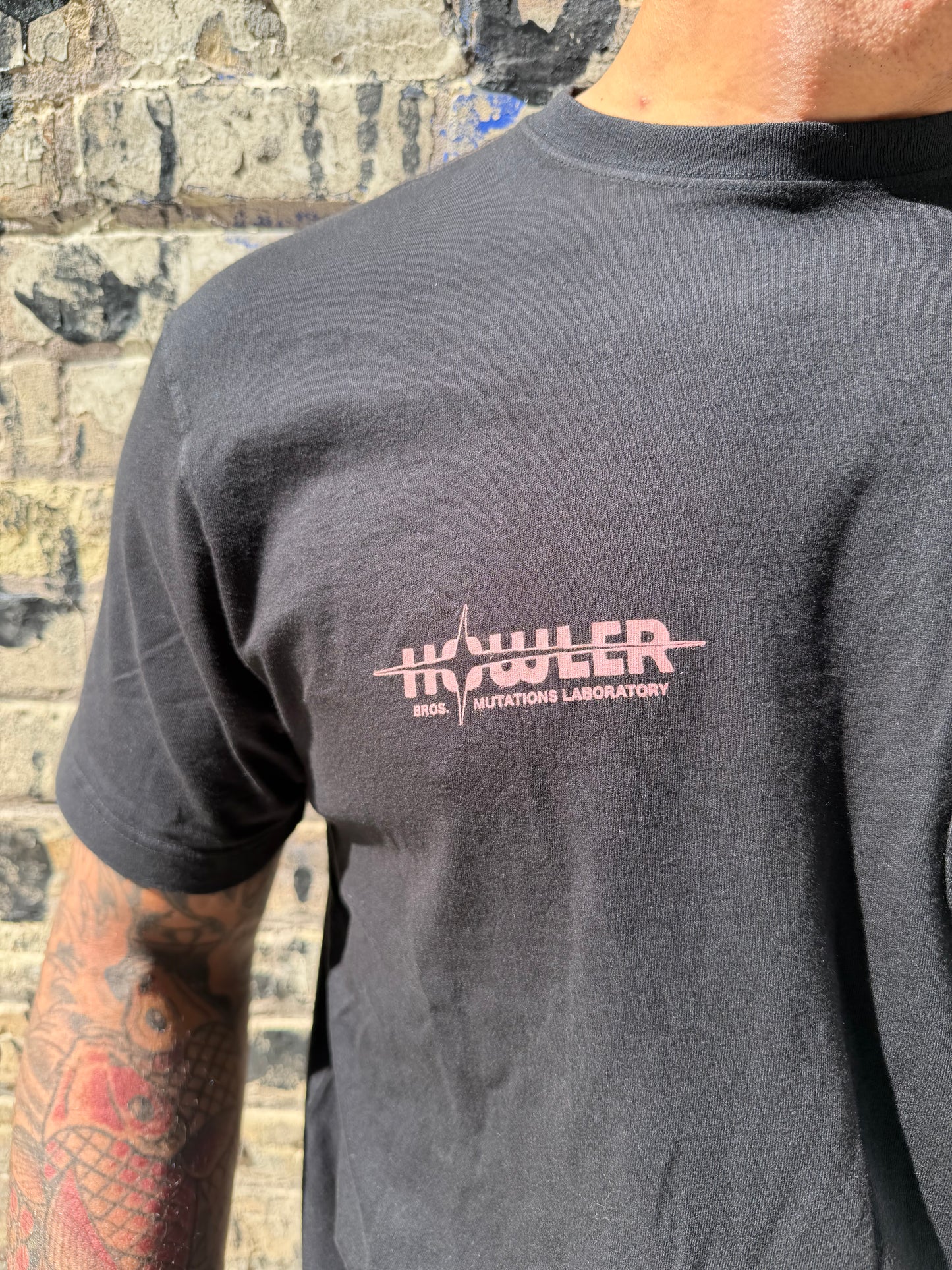 Person wearing a black shirt with a logo on the chest, standing on a textured surface.