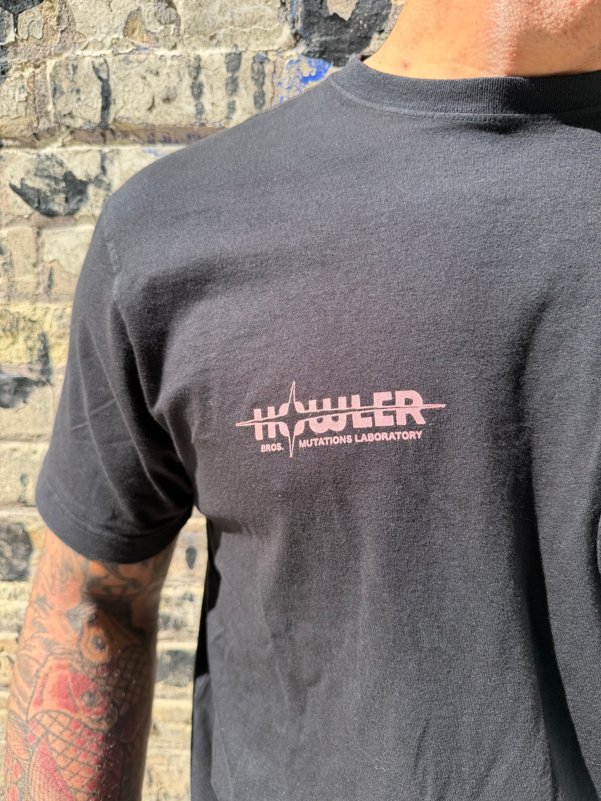 Person wearing a black shirt with a logo on the chest, standing on a textured surface.