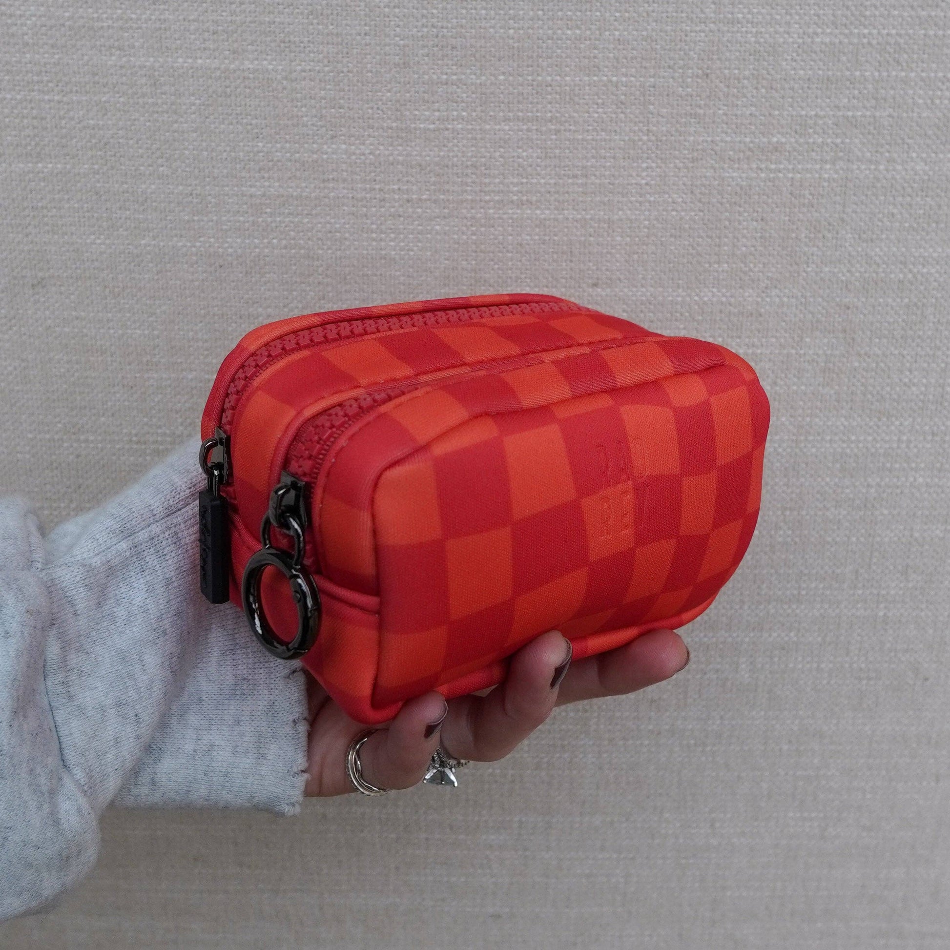 Red checkered pouch held by a person against a gray background