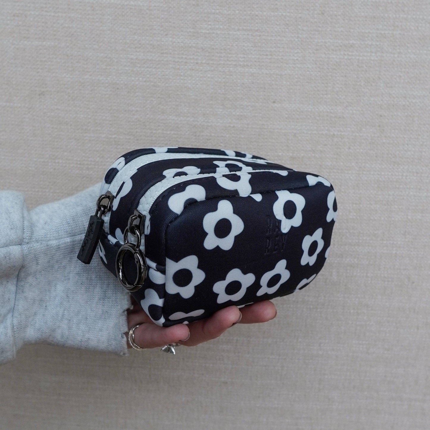 Black pouch with white floral pattern held by a person against a neutral background