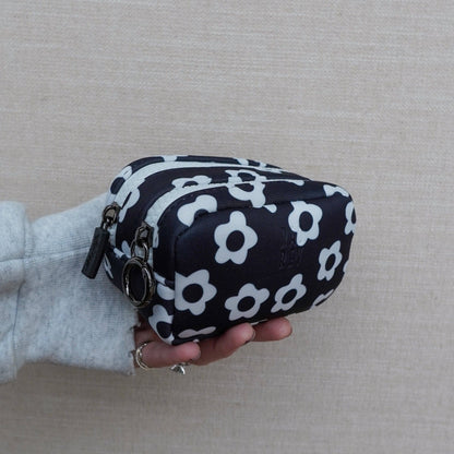Black pouch with white floral pattern held by a person against a neutral background