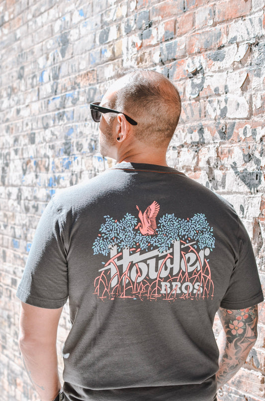 Man wearing a dark gray t-shirt with 'Hooters Bros' design against a brick wall.