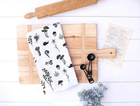 White towel with black floral pattern on a wooden cutting board with a rolling pin and book.