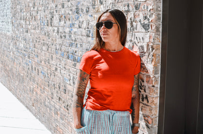 Person wearing a red shirt and sunglasses standing against a brick wall.