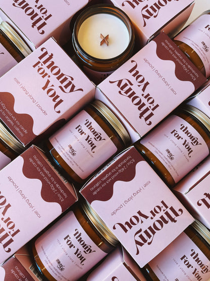 Jars and boxes of 'Thorny For You' products with candles on a patterned background.