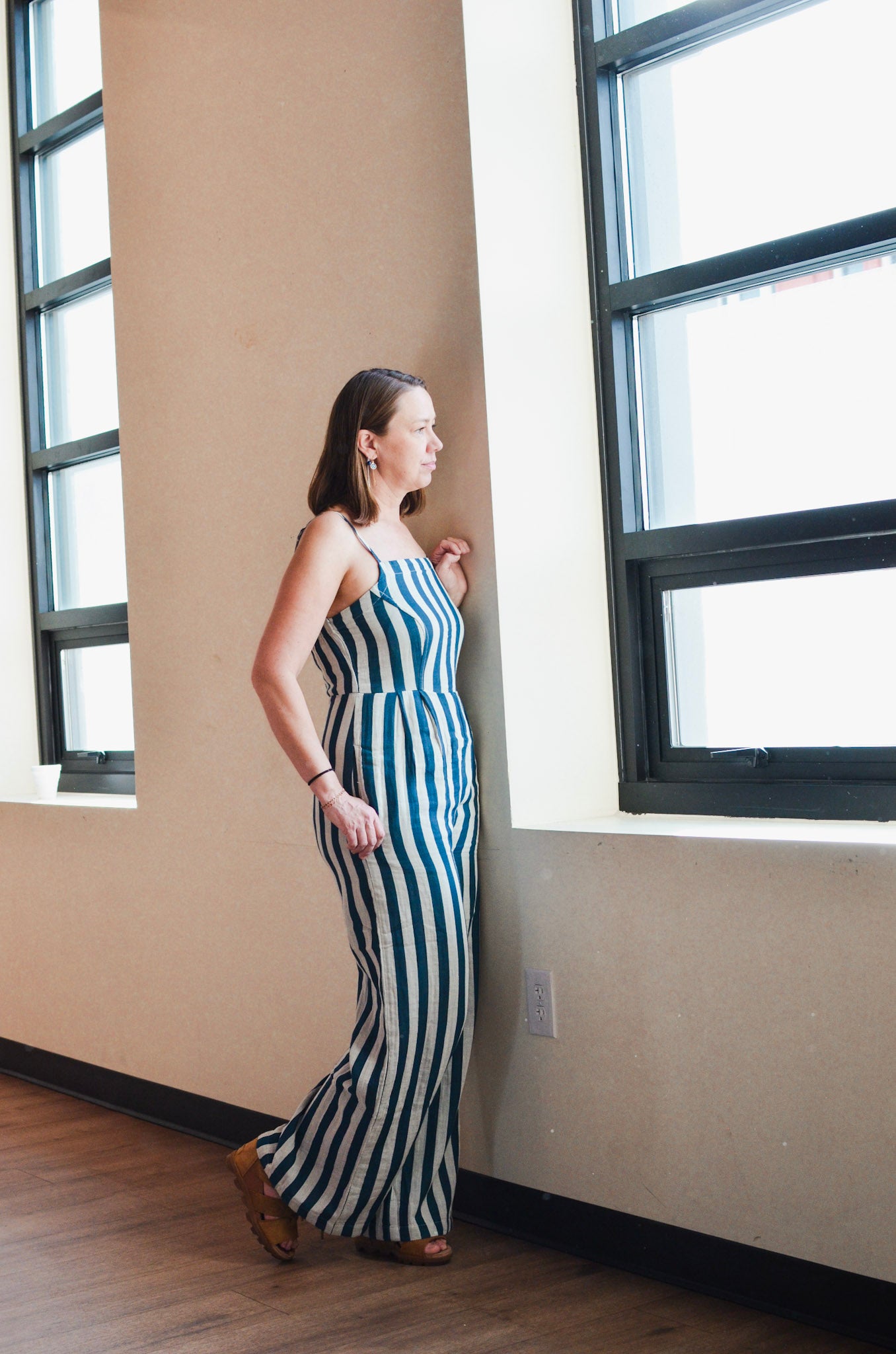 Woman in a striped dress standing by a window in a room with beige walls.
