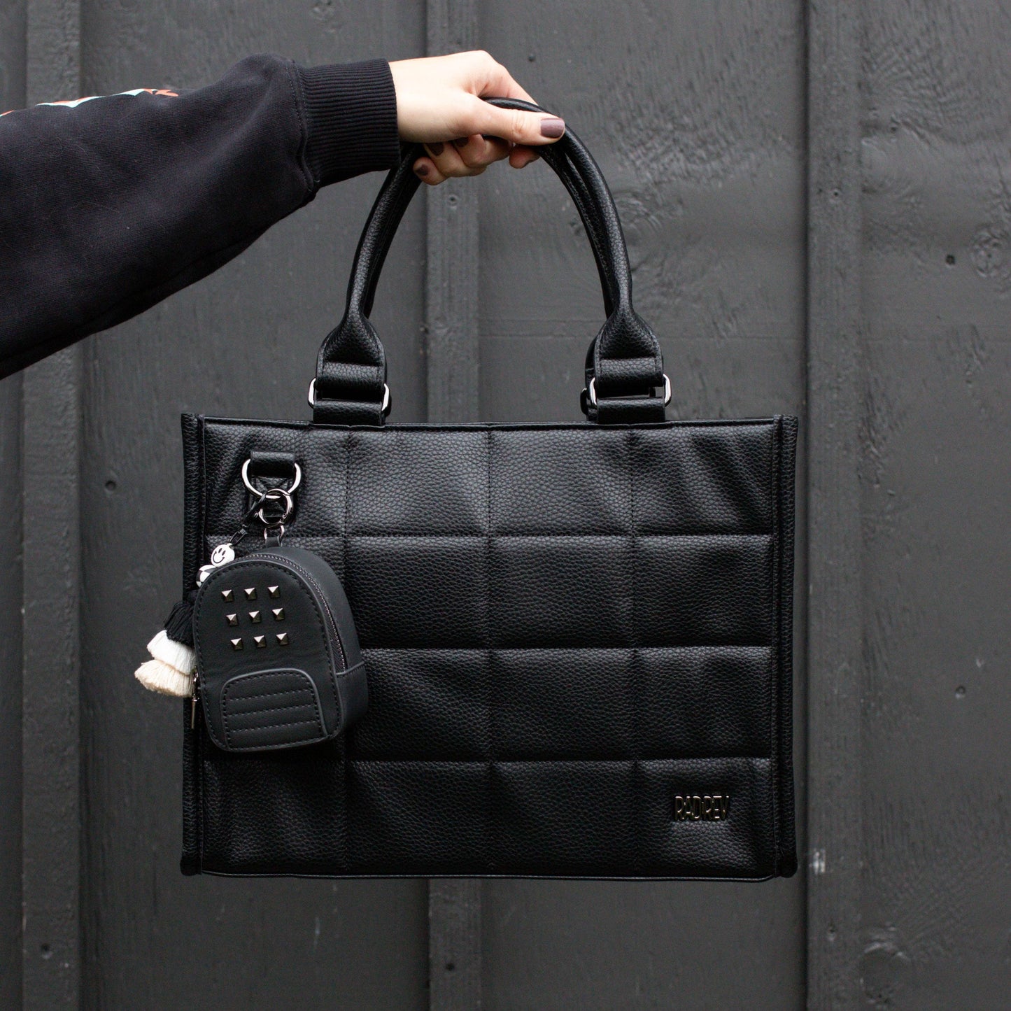 Black quilted handbag with a keychain held by a person against a dark background