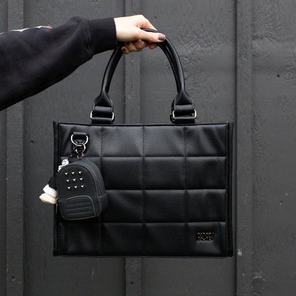 Black quilted handbag with a keychain held by a person against a dark background