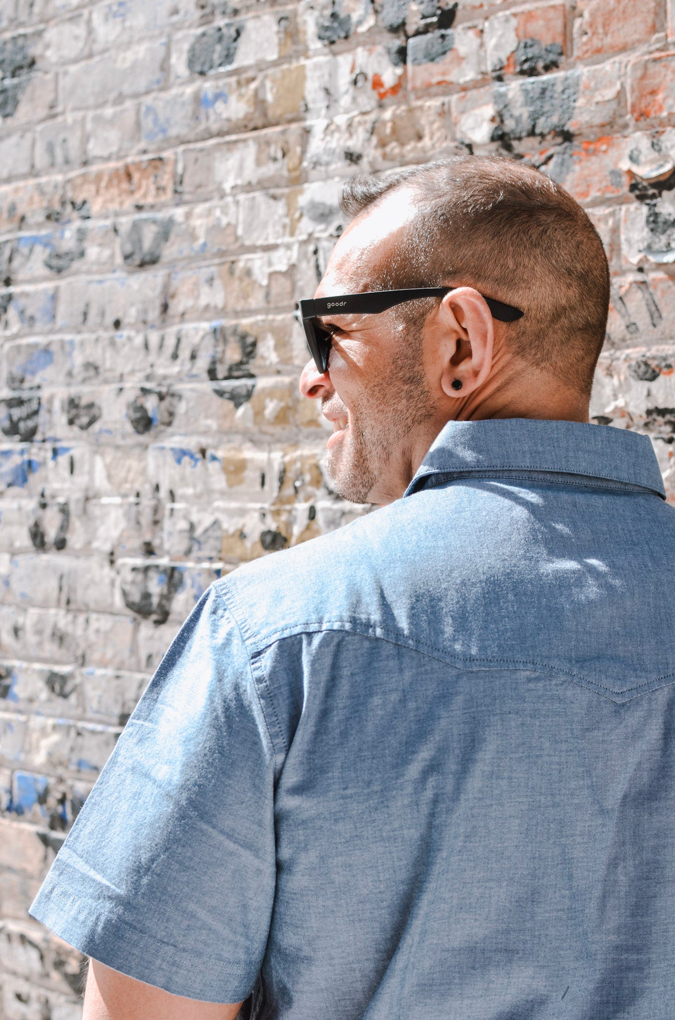 Man wearing sunglasses and a blue shirt against a brick wall