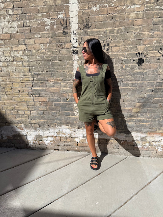 Woman in a green romper standing against a brick wall.