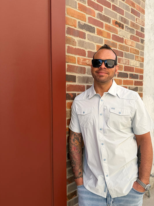 Man wearing sunglasses and a white shirt on a brick surface