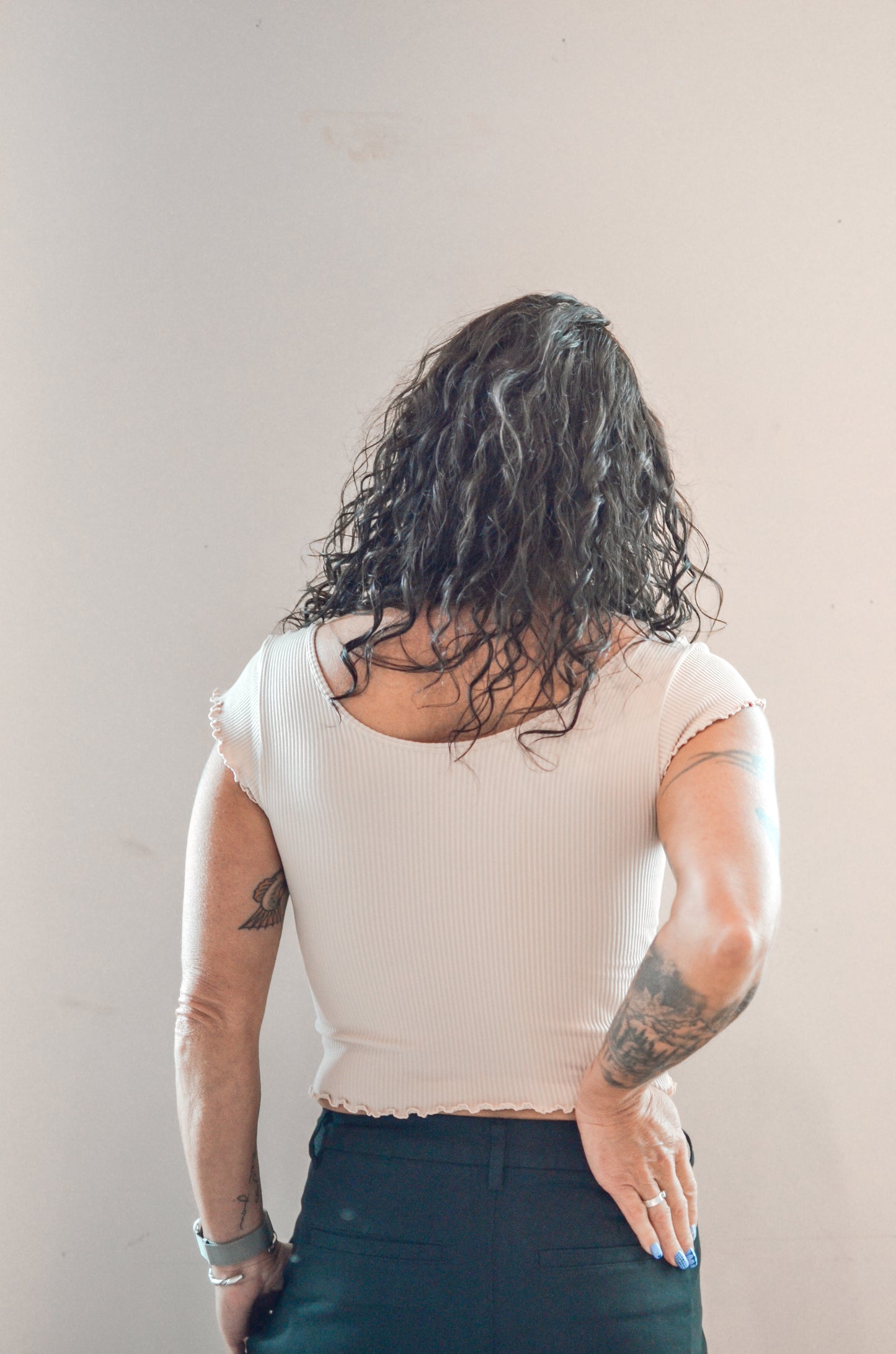 Person wearing a beige top and dark pants against a plain background