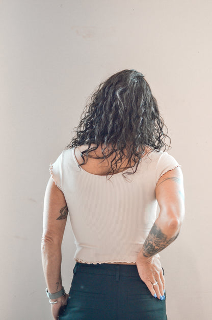 Person wearing a beige top and dark pants against a plain background