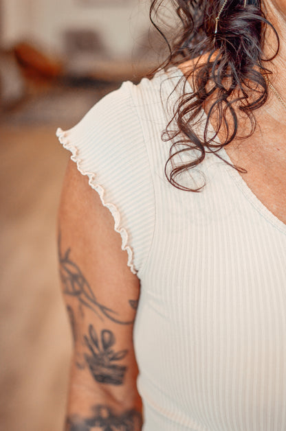 Person wearing a white sleeveless top with lace trim, showing tattoos on the arm.