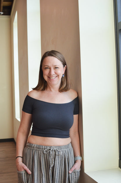 Woman wearing a black top and patterned pants standing indoors.
