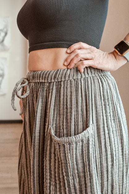 Person wearing a dark ribbed top and striped pants with a blurred background