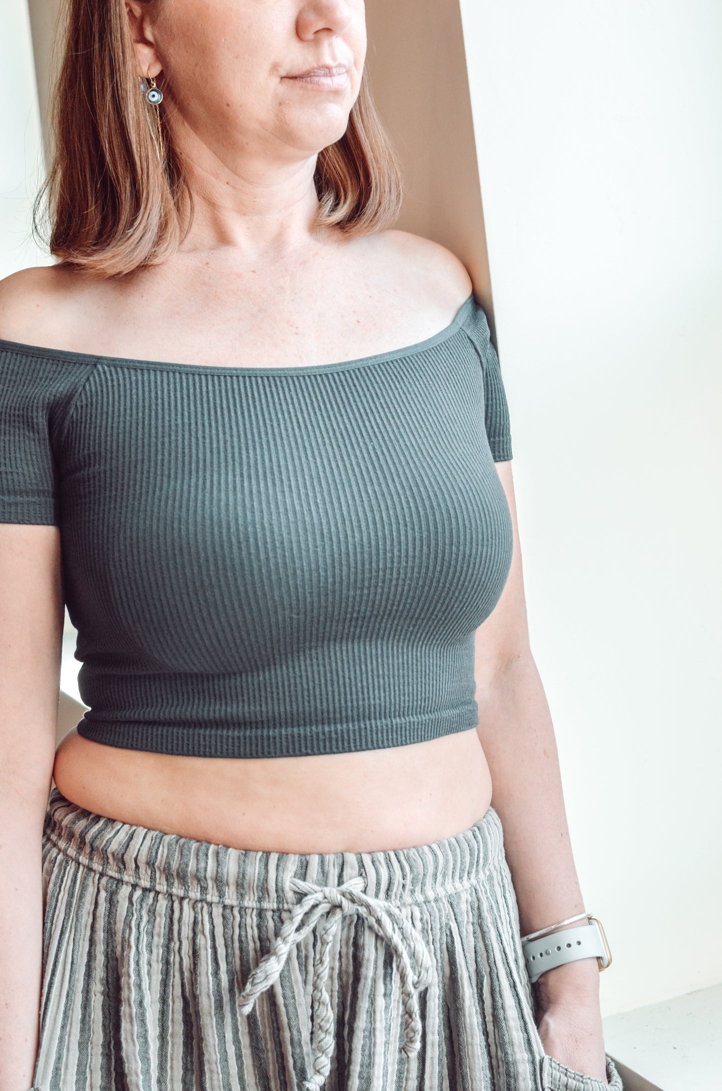 Woman wearing a green off-shoulder top and plaid pants against a neutral background