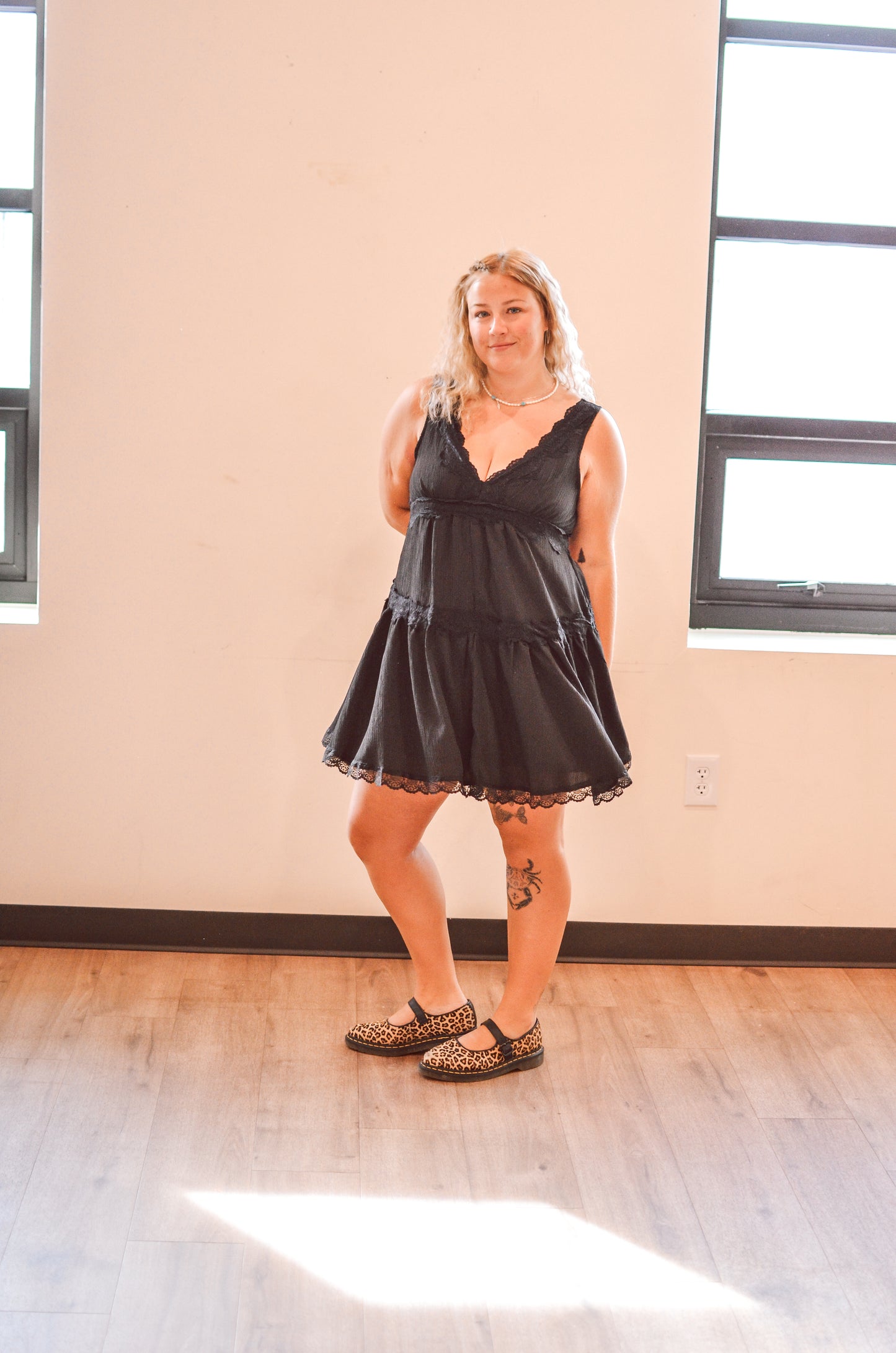 Woman wearing a black lace dress standing in a room with large windows.