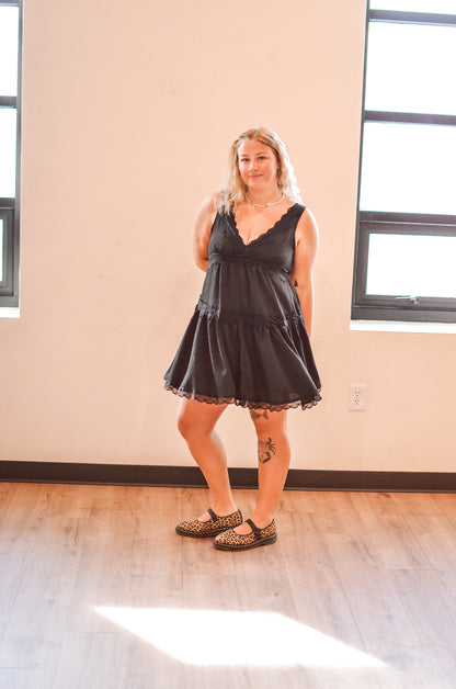Woman wearing a black lace dress standing in a room with large windows.