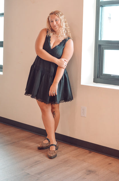 Woman in a black dress standing in a room with beige walls and wooden flooring.