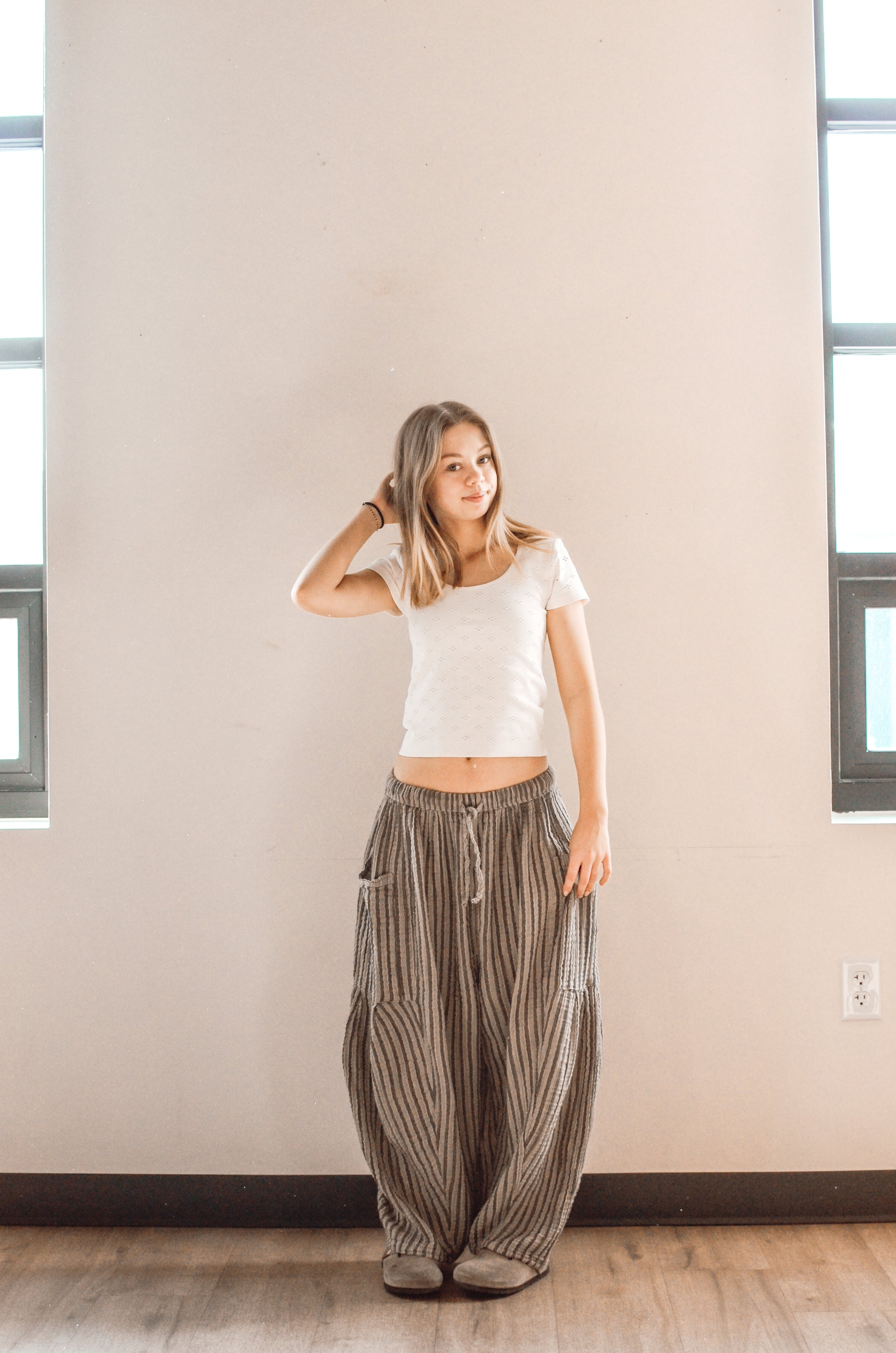 Woman wearing a white top and patterned pants standing against a plain wall.