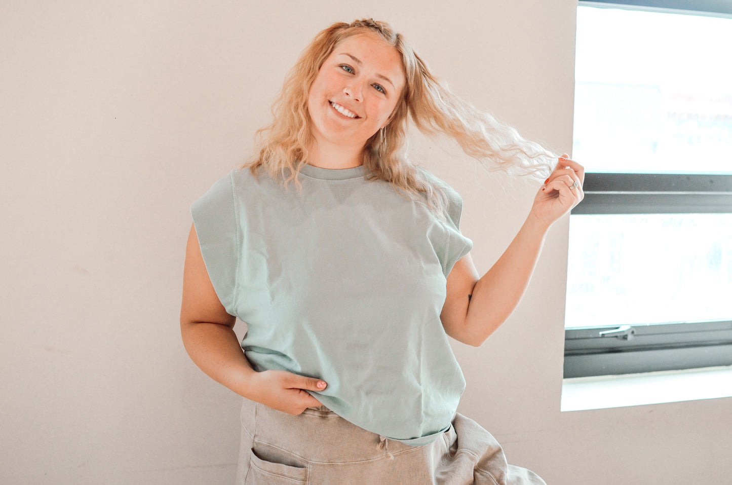 Woman wearing a light blue shirt and beige pants, standing indoors with a neutral background.