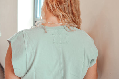 Person wearing a light green sleeveless top with a neutral background