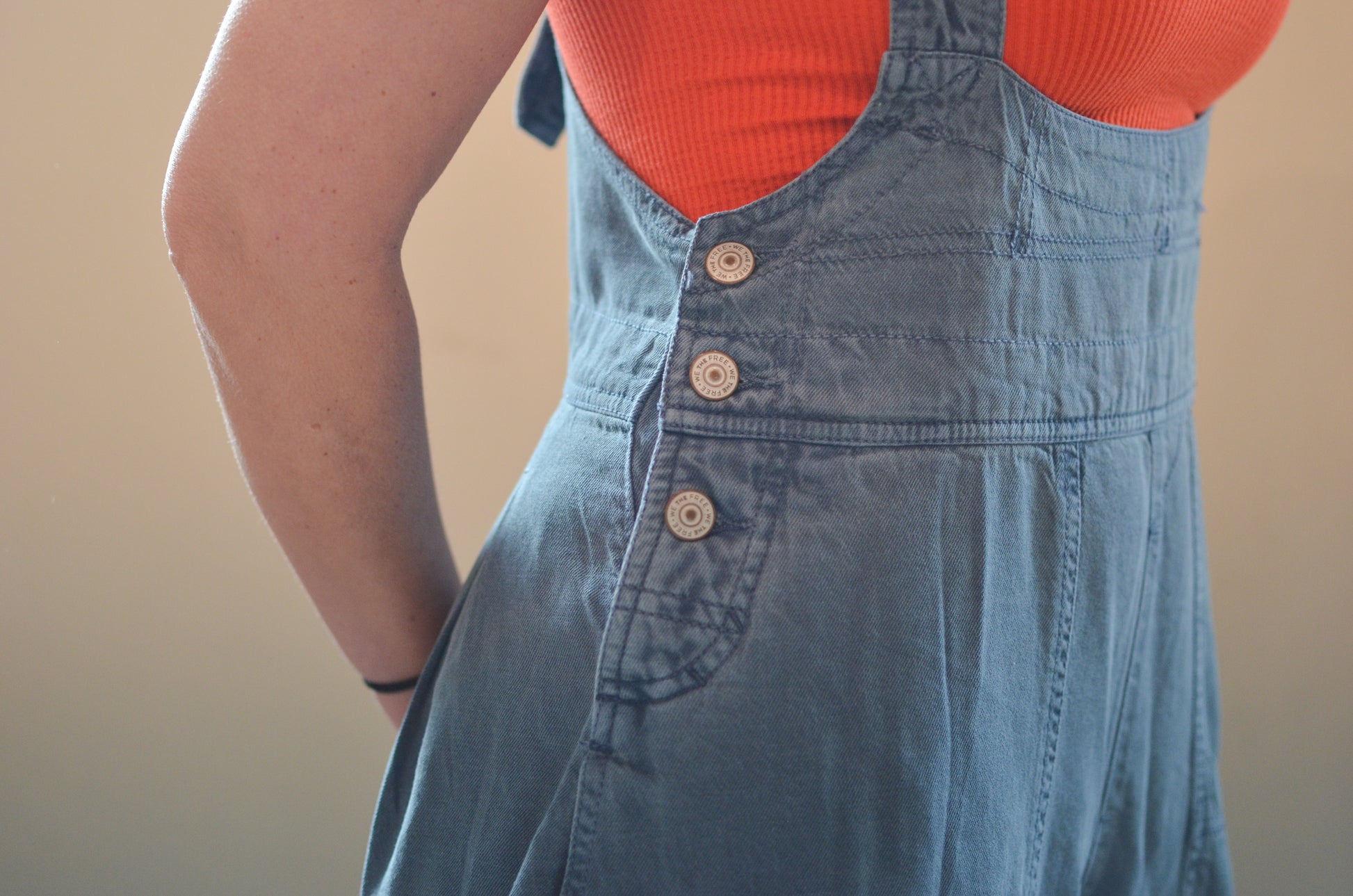 Person wearing a blue denim dress over an orange top against a beige background