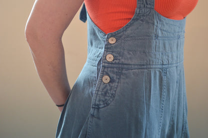 Person wearing a blue denim dress over an orange top against a beige background