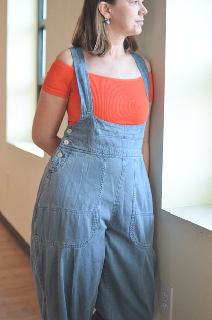 Woman wearing denim overalls and an orange top indoors.