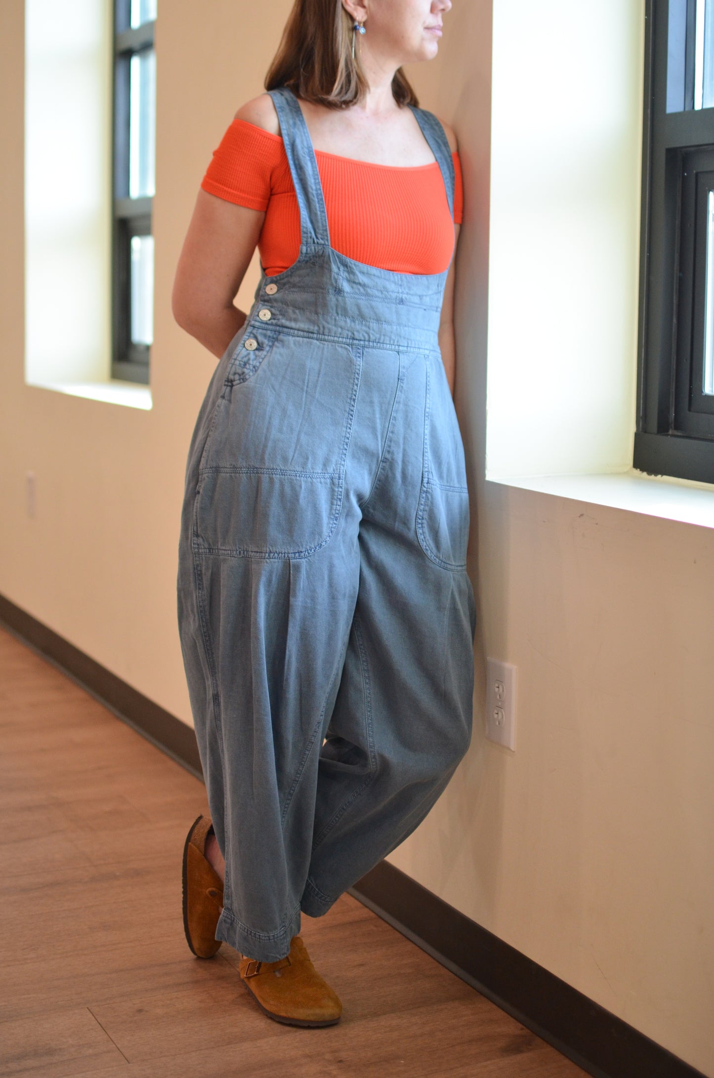 Person wearing a red top and blue denim overalls standing indoors.