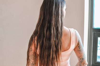 Woman with long hair and tattoos wearing a sleeveless top, standing indoors.