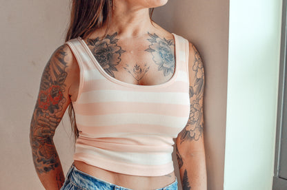 Person wearing a peach striped tank top with visible tattoos on arms and neck.