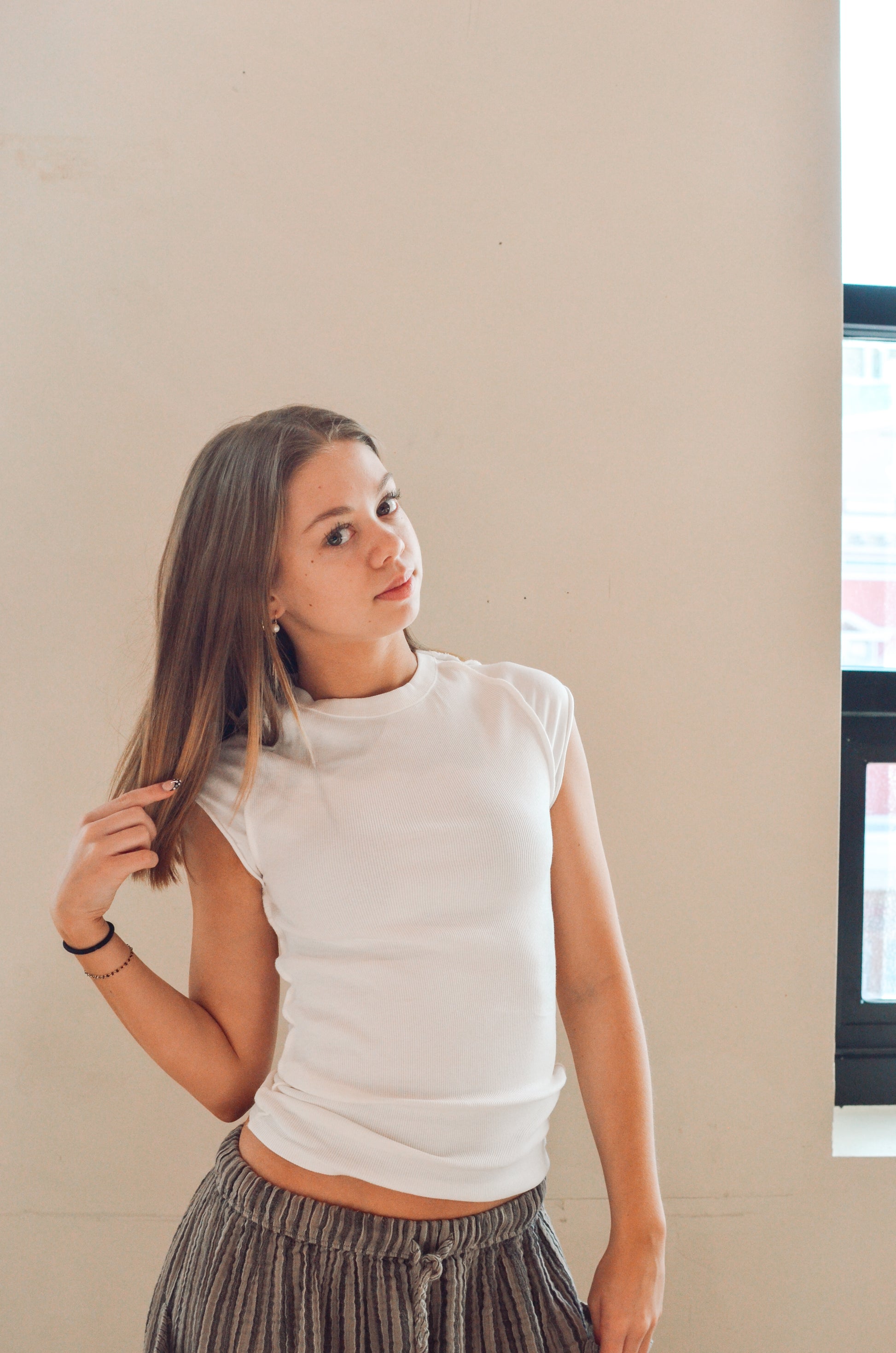 Woman wearing a white sleeveless top and patterned pants against a beige wall.