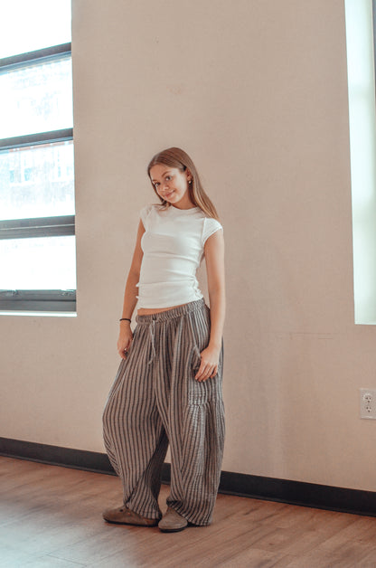 Woman wearing a white top and striped pants standing in a room with a neutral wall and wooden floor.