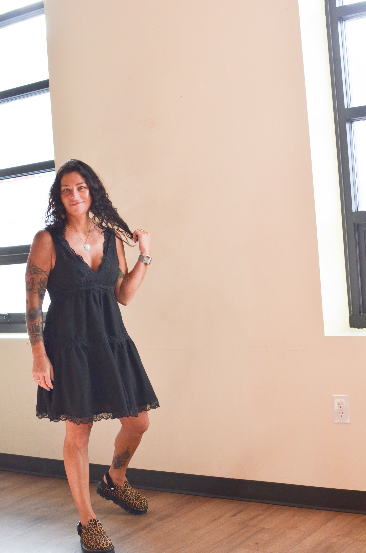 Woman wearing a black dress standing in a room with beige walls and a window.