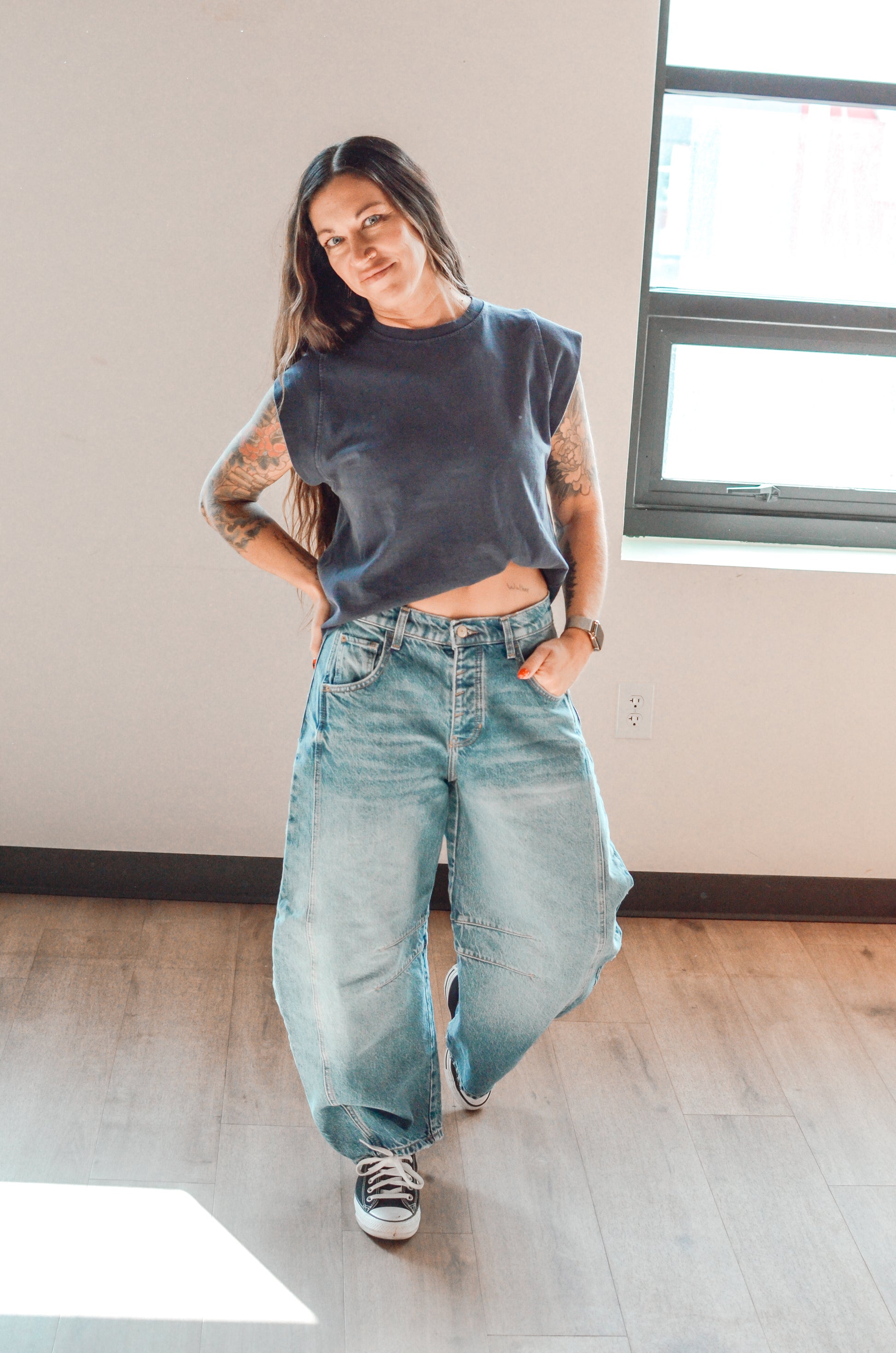 Woman wearing a sleeveless top and wide-leg jeans in a room with a window.