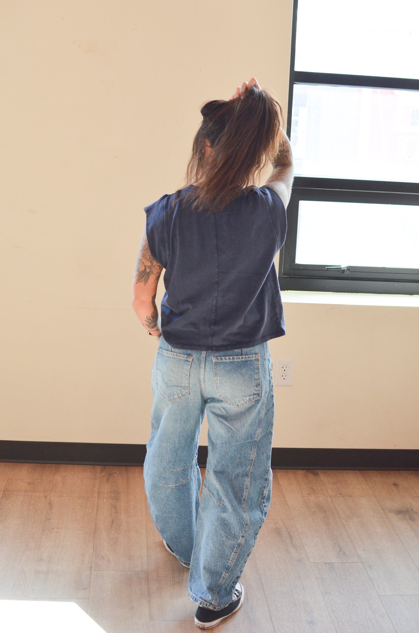 Person wearing a blue shirt and jeans standing in a room with a window.