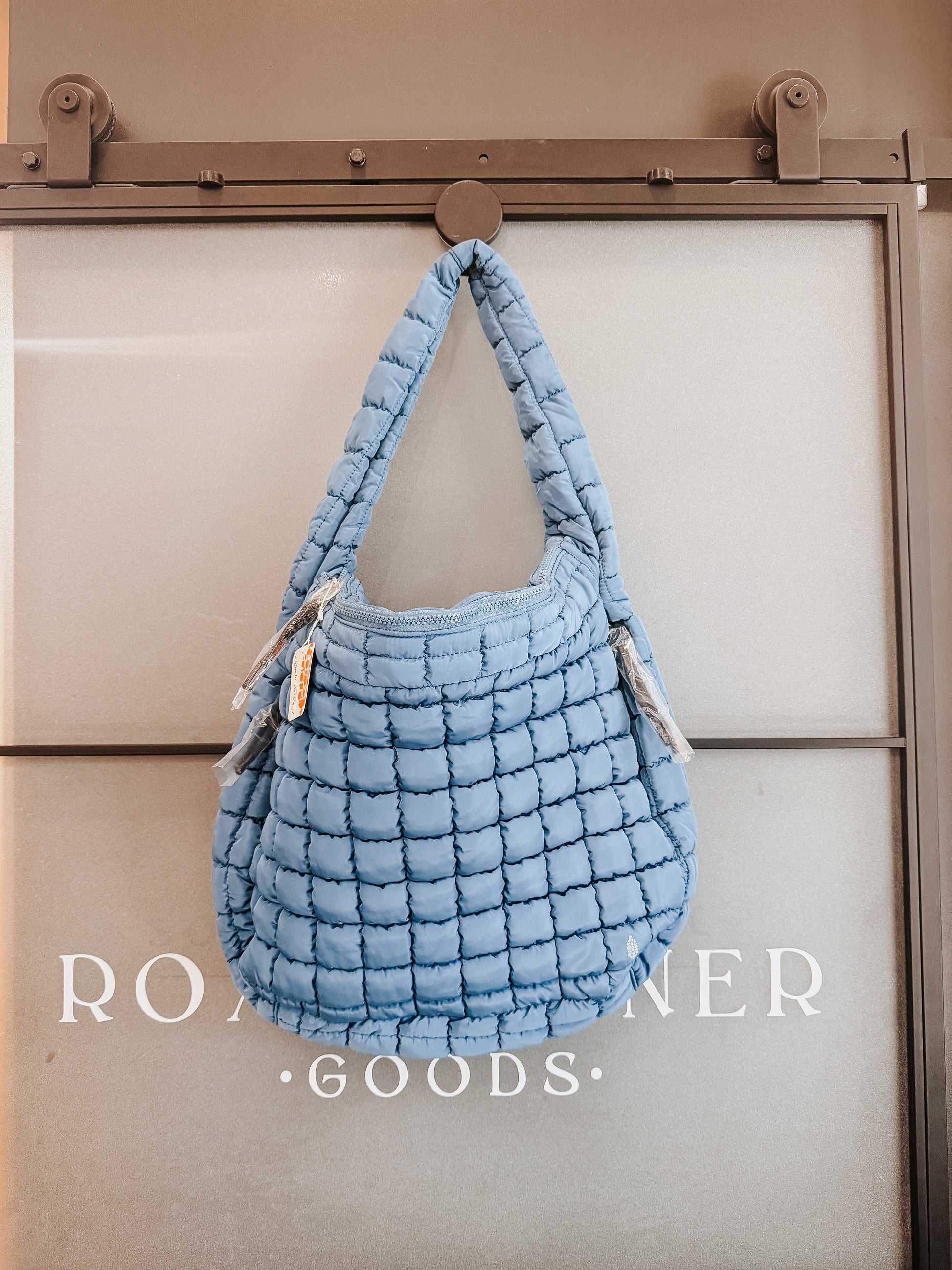 Blue textured handbag hanging on a door with 'Room & Board' branding.