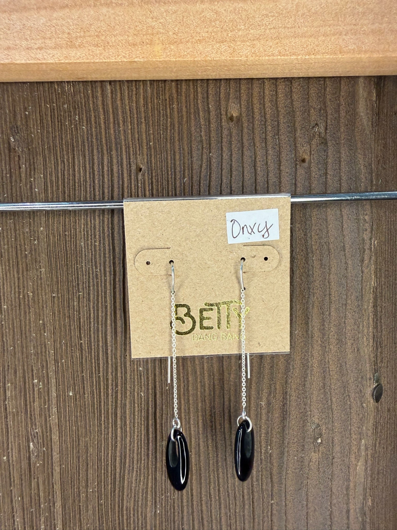 Pair of earrings on a 'Bella' branded card against a wooden background