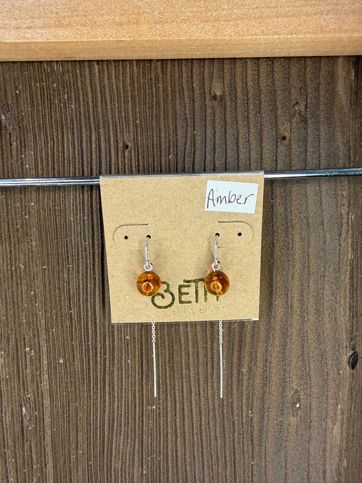Amber earrings on a cardboard backing with 'Beti' branding against a wooden background