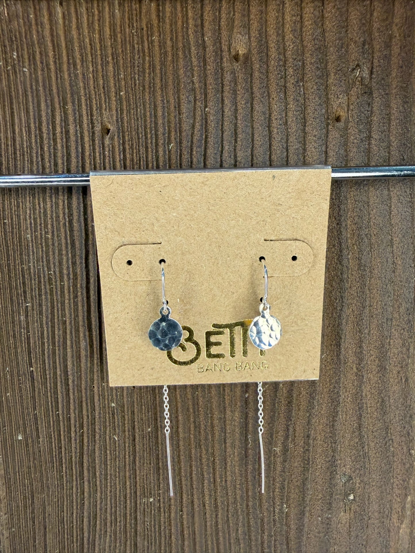 Pair of earrings on a cardboard backing with 'Beti' branding against a wooden background