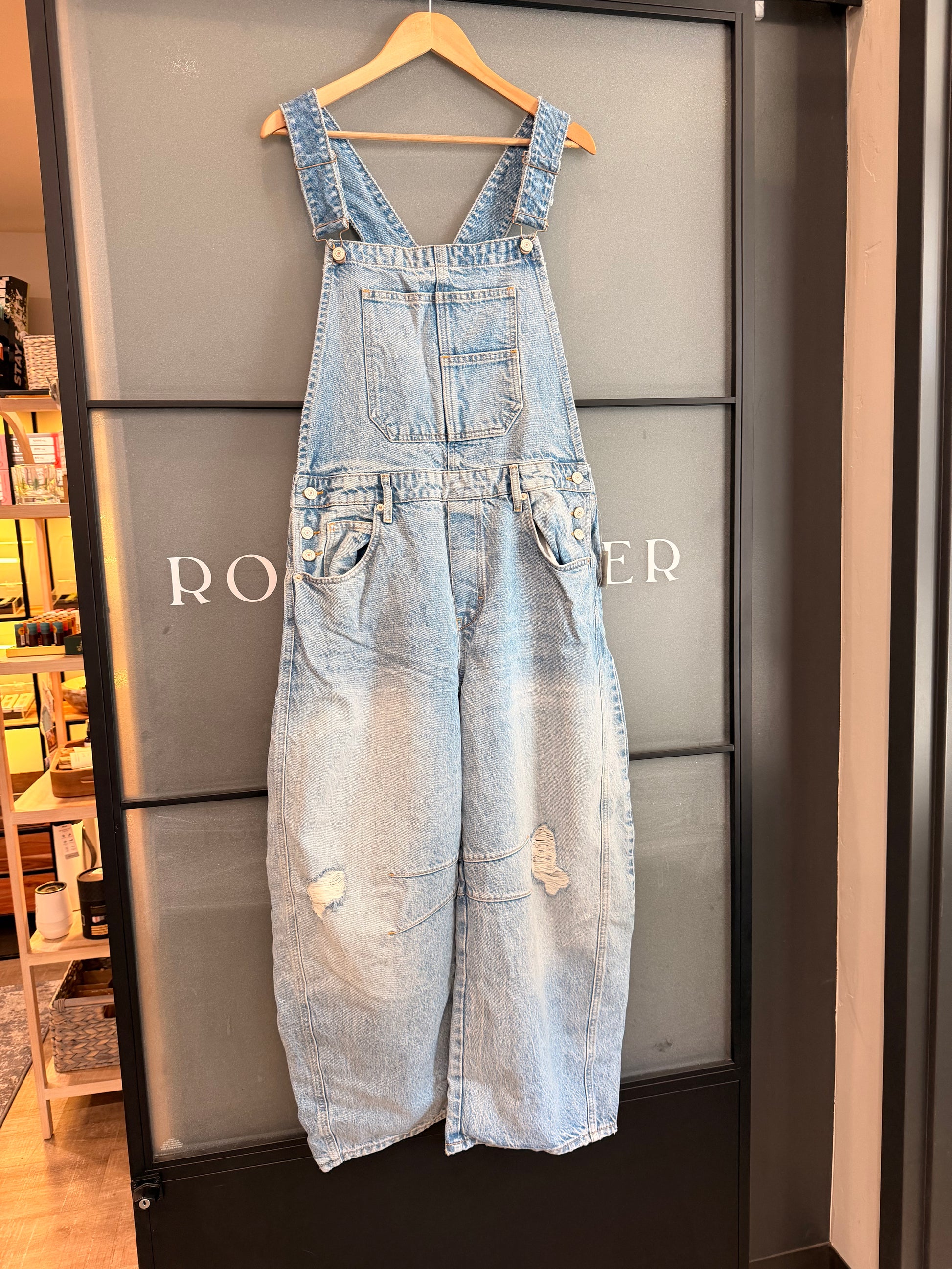 Denim overalls on a hanger against a branded background