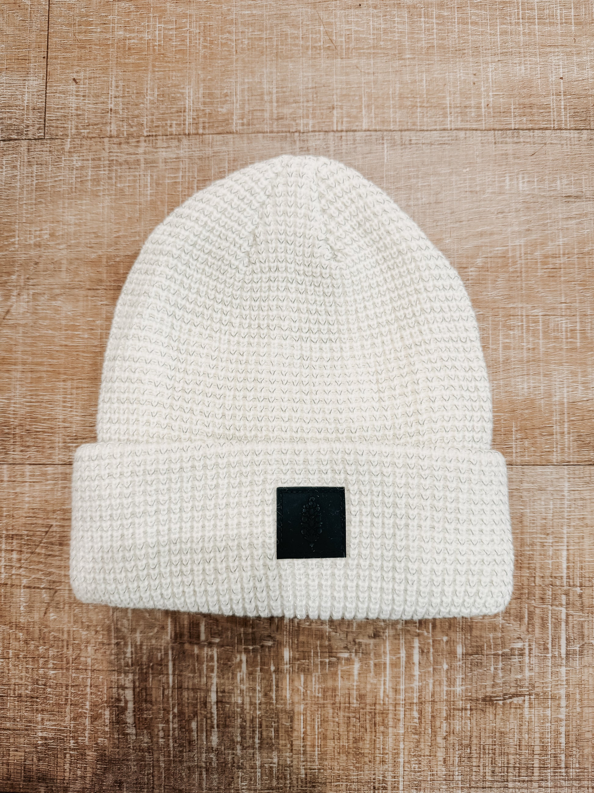 White beanie with a black patch on a wooden surface