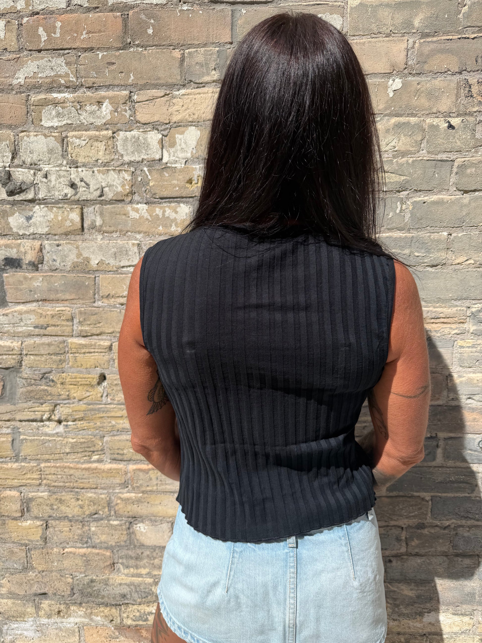 Person wearing a black sweater and light blue shirt on a brick pavement