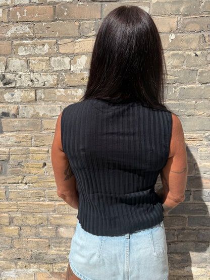 Person wearing a black sweater and light blue shirt on a brick pavement