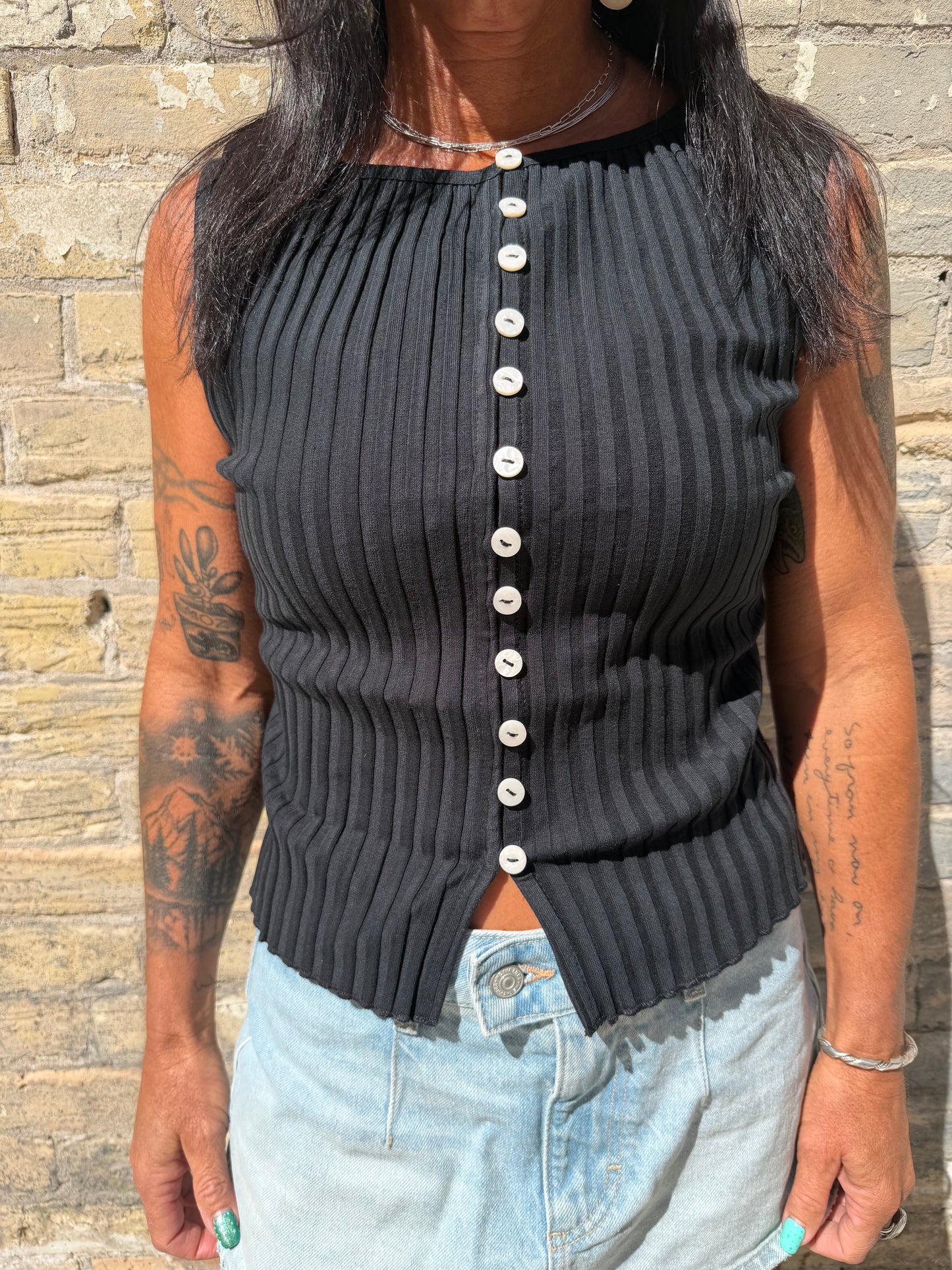 Black ribbed sweater with pearl buttons worn by a person on a stone surface