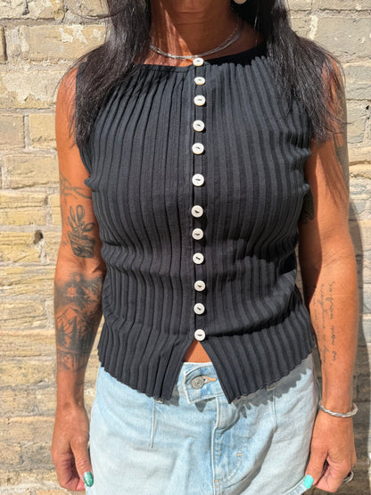 Black ribbed sweater with pearl buttons worn by a person on a stone surface